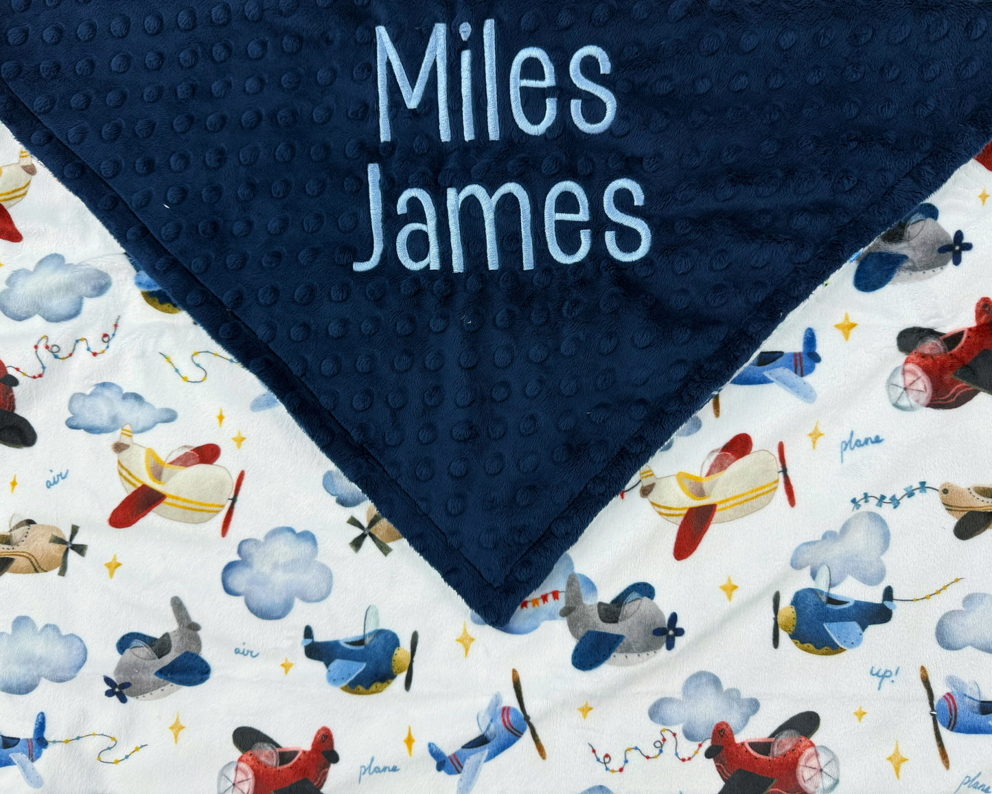 Navy blue minky dot blanket with airplane pattern and embroidered names on a white background