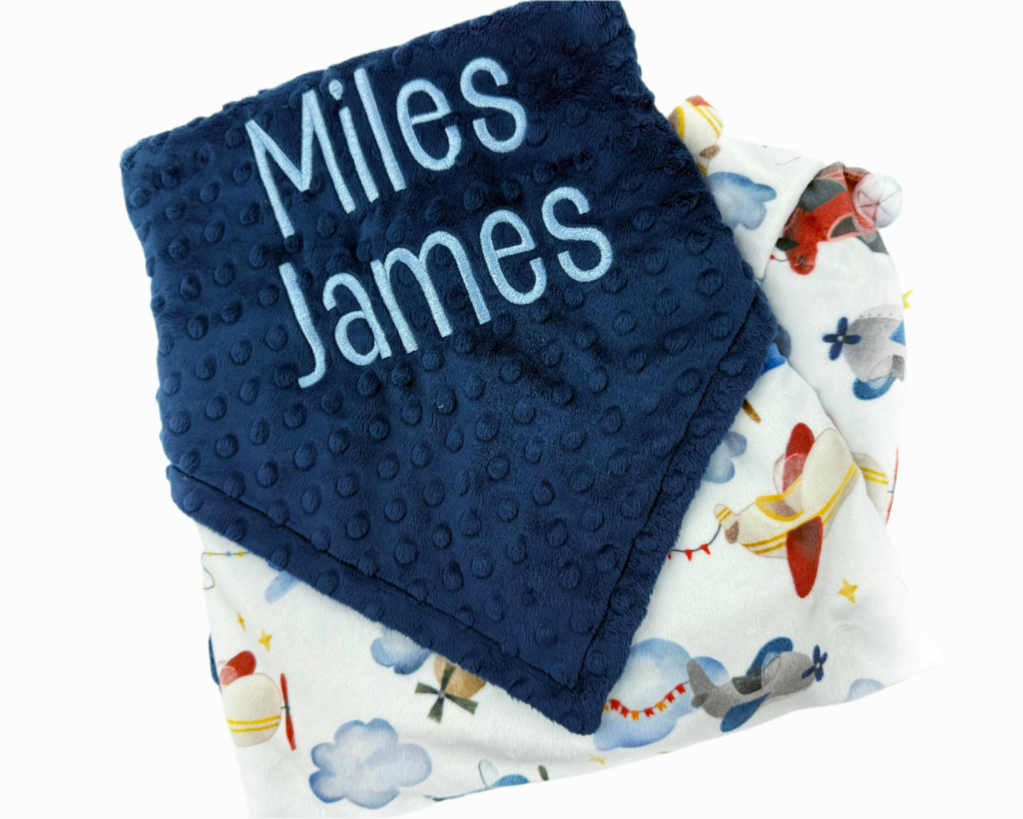 Navy blue textured blanket with 'Miles James' text and a patterned airplane blanket underneath.