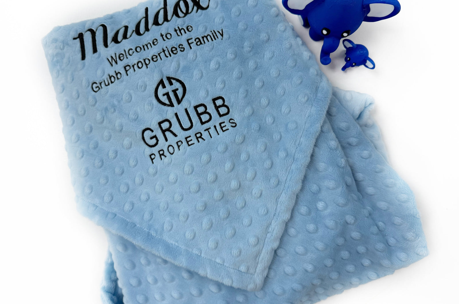 Folded minky baby blanket with a custom embroidered business logo in the corner, showcasing a branded company gift.
