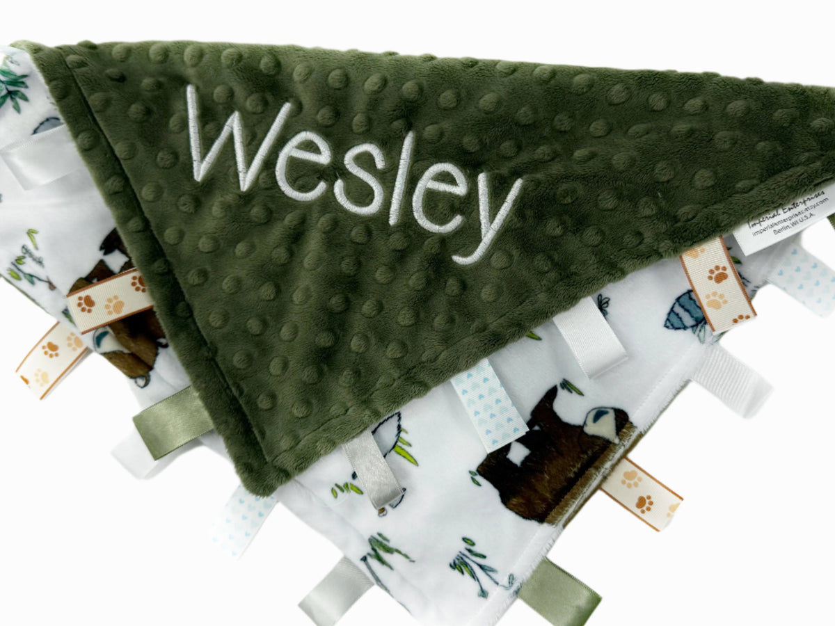 Green textured blanket with 'Wesley' embroidered on it, surrounded by other baby items on a white background.