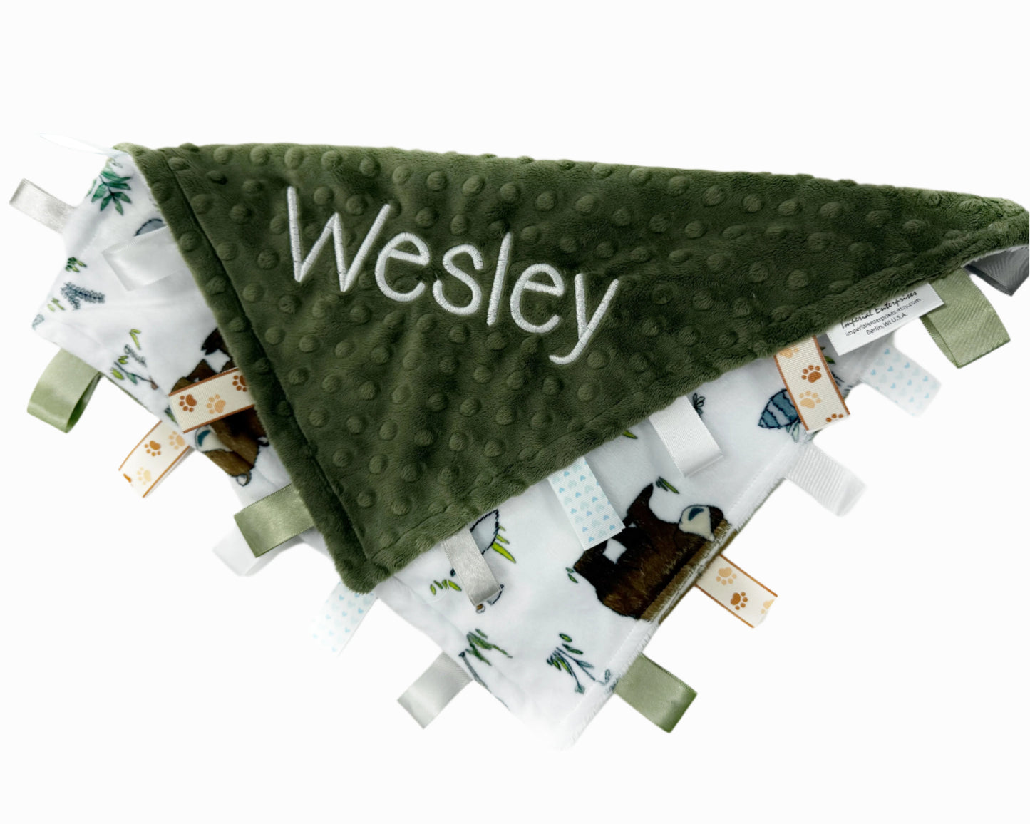 Green textured blanket with 'Wesley' embroidered on it, surrounded by other baby items on a white background.