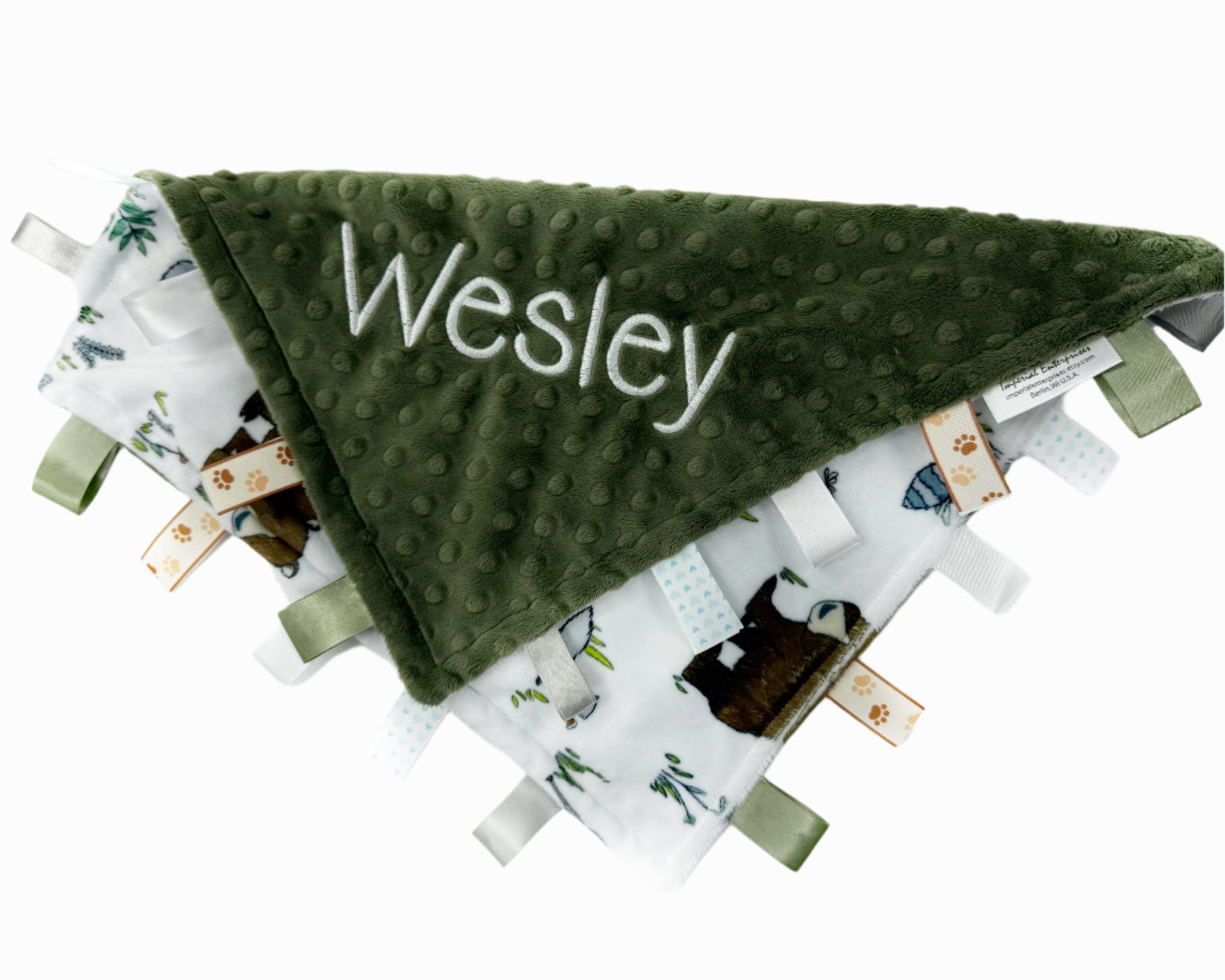 Green textured blanket with 'Wesley' embroidered on it, surrounded by other baby items on a white background.