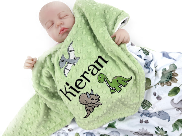 Baby wrapped in a green blanket with dinosaur designs and the name 'Kieran'.
