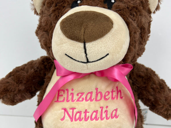 A personalized brown teddy bear with a name and birth date printed on its chest, adorned with a pink ribbon.