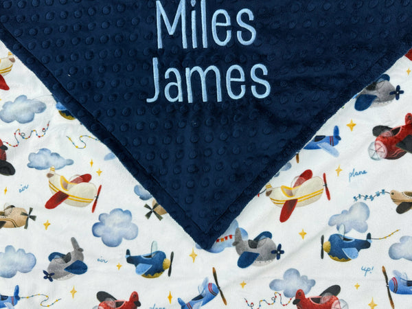 Navy blue minky dot blanket with airplane pattern and embroidered names on a white background
