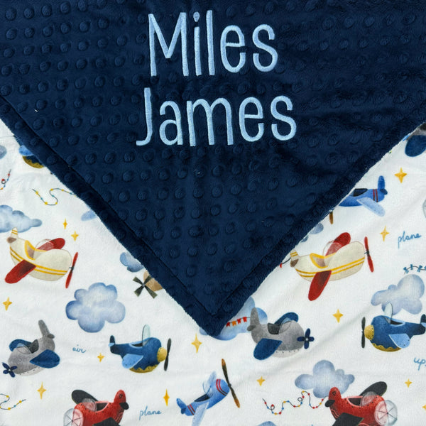Navy blue minky dot blanket with airplane pattern and embroidered names on a white background