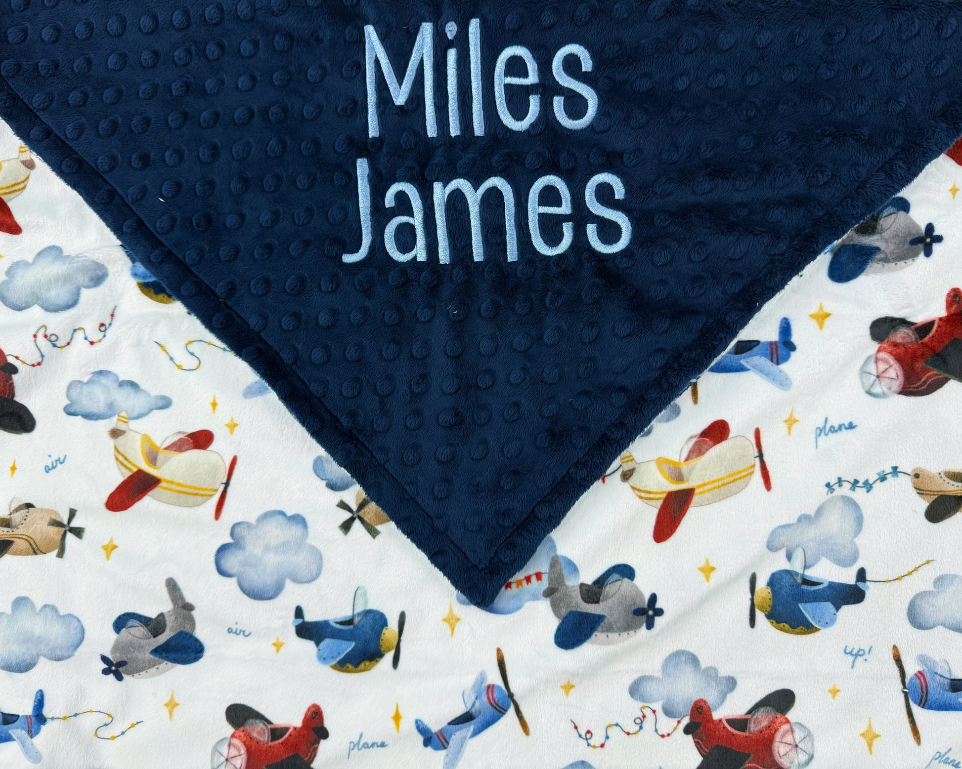 Navy blue minky dot blanket with airplane pattern and embroidered names on a white background