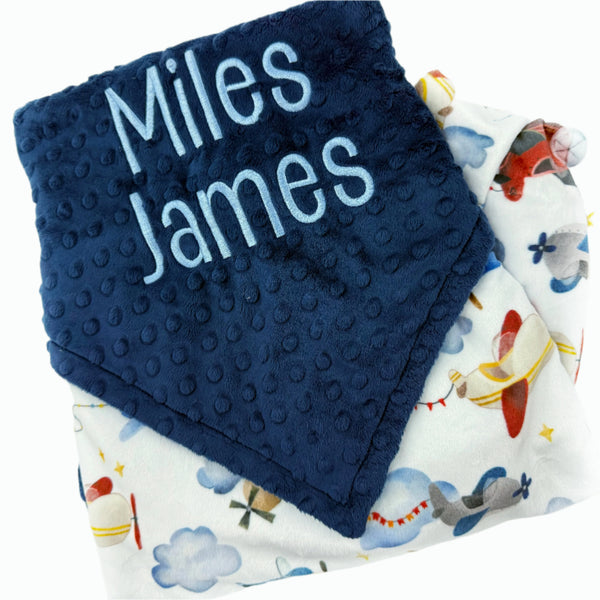 Navy blue textured blanket with 'Miles James' text and a patterned airplane blanket underneath.