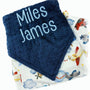 Navy blue textured blanket with 'Miles James' text and a patterned airplane blanket underneath.