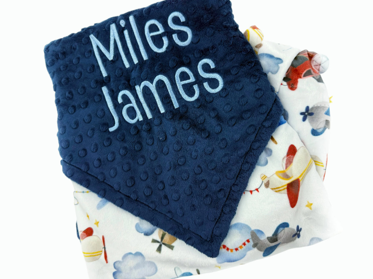 Navy blue textured blanket with 'Miles James' text and a patterned airplane blanket underneath.