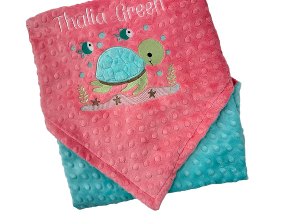 Pink and blue baby blanket with turtle design and 'Thalia Green' text on a white background