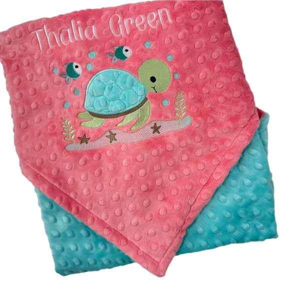 Pink and blue baby blanket with turtle design and 'Thalia Green' text on a white background