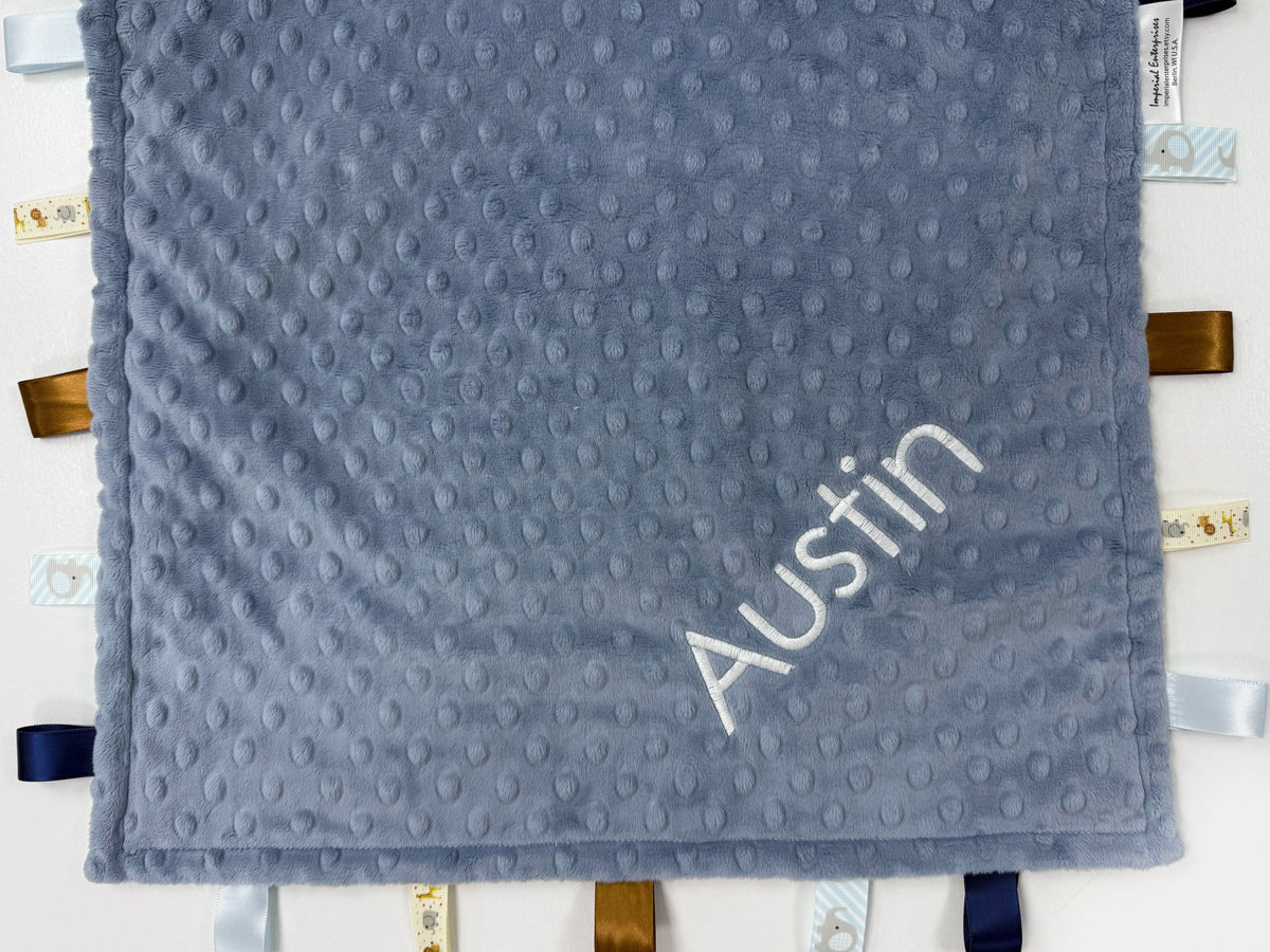 Gray textured blanket with 'Austin' embroidered on it, hanging on a white wall.