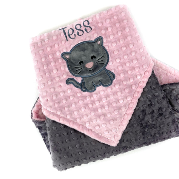 A minky baby blanket with one side pink and the other gray, featuring an embroidered name 'Tess' on the pink side and an appliqued gray kitten.