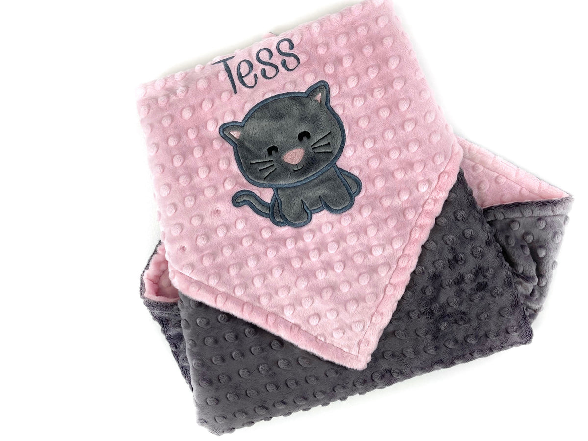 A minky baby blanket with one side pink and the other gray, featuring an embroidered name 'Tess' on the pink side and an appliqued gray kitten.