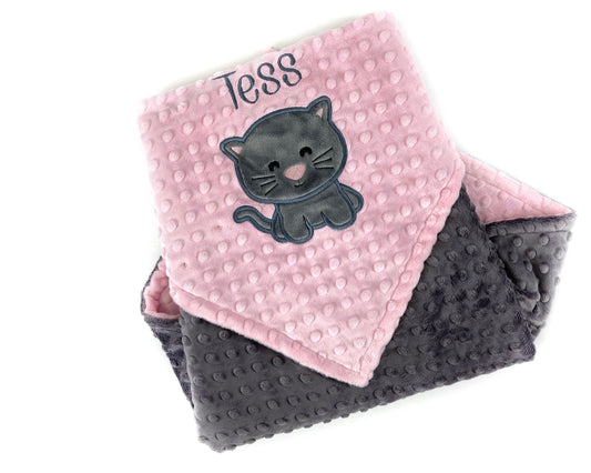 A minky baby blanket with one side pink and the other gray, featuring an embroidered name 'Tess' on the pink side and an appliqued gray kitten.