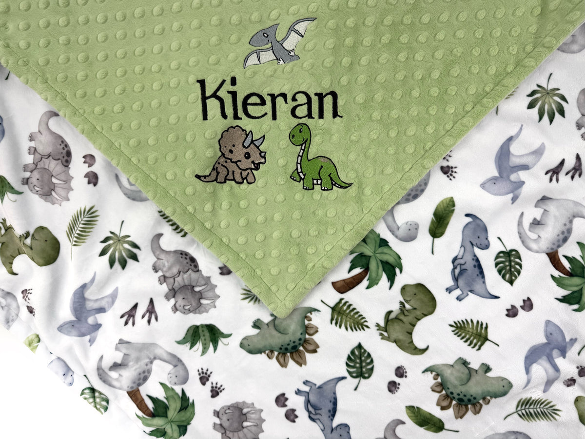 Personalized dinosaur baby blanket with embroidered baby name on sage green dimple minky and colorful dinosaur print backing