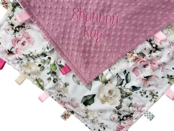 Floral baby blanket with textured pink corner and embroidered name on a white background