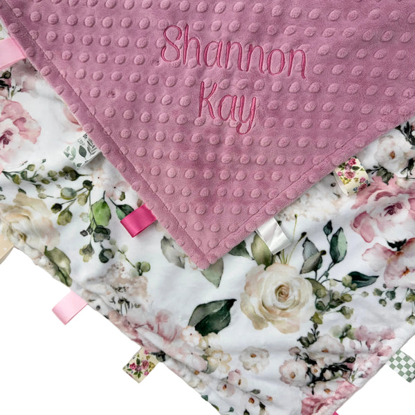 Floral baby blanket with textured pink corner and embroidered name on a white background