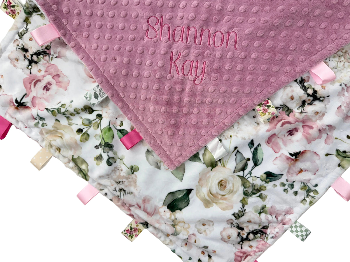 Floral baby blanket with textured pink corner and embroidered name on a white background