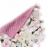 Floral-patterned tag blanket with pink textured border and ribbons on a white background